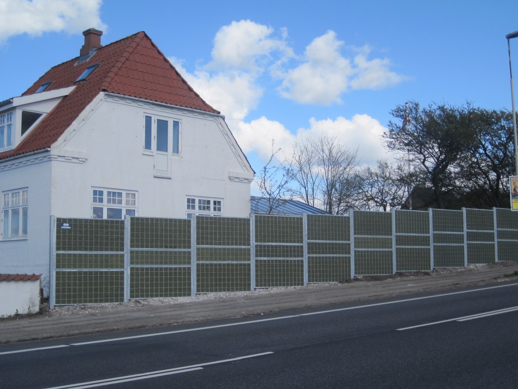 Et Noistop® Steel støjhegn fra Poda Hegn opsat foran et hus ved en hovedvej til afskærmning af trafikstøj